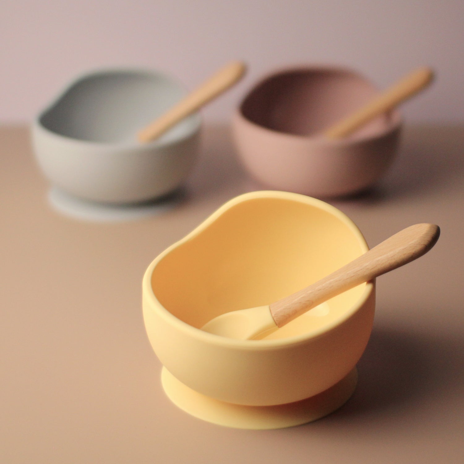 baby feeding silicone suction bowl in maroon, grey and yellow, with matching wooden handle spoon